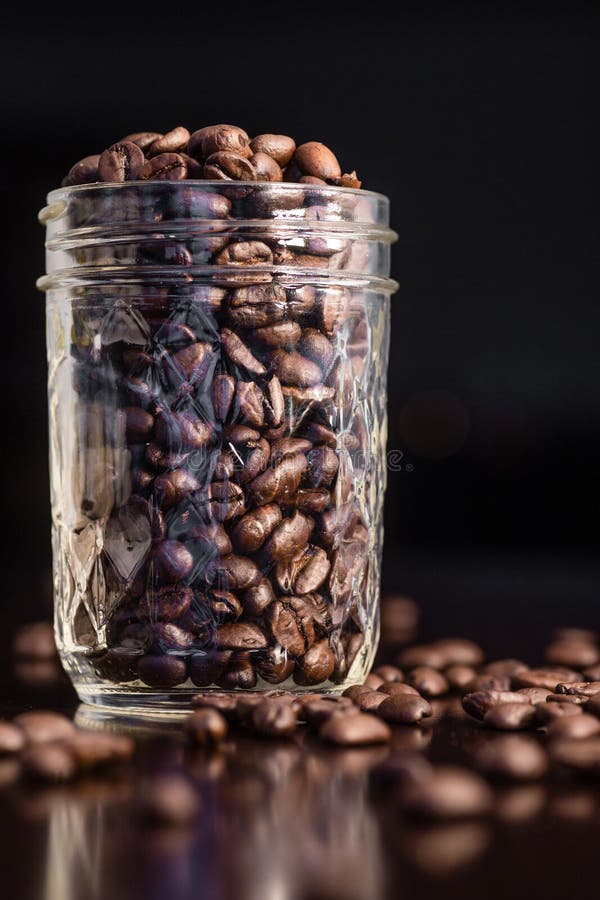 Mason jar of rich dark coffee beans, spilled out onto a table. Great for coffee houses, homes and coffee drinkers. Mason jar of rich dark coffee beans, spilled out onto a table. Great for coffee houses, homes and coffee drinkers