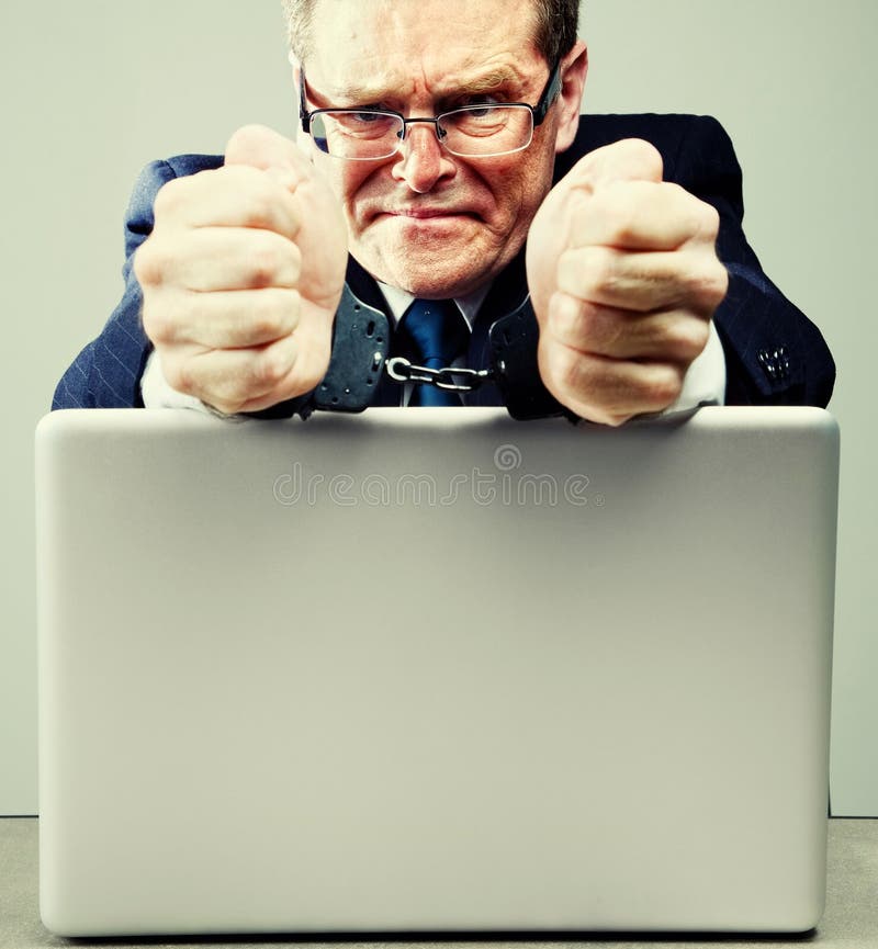 Businessman in handcuffs at desk with laptop computer. Businessman in handcuffs at desk with laptop computer