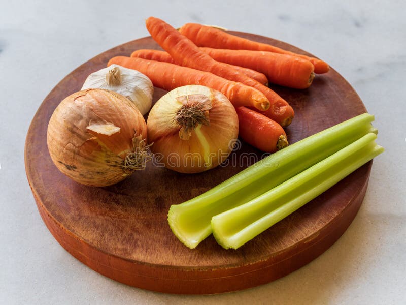 View of raw vegetables mirepox ingredients – onions, celery and carrots on a wooden board. View of raw vegetables mirepox ingredients – onions, celery and carrots on a wooden board
