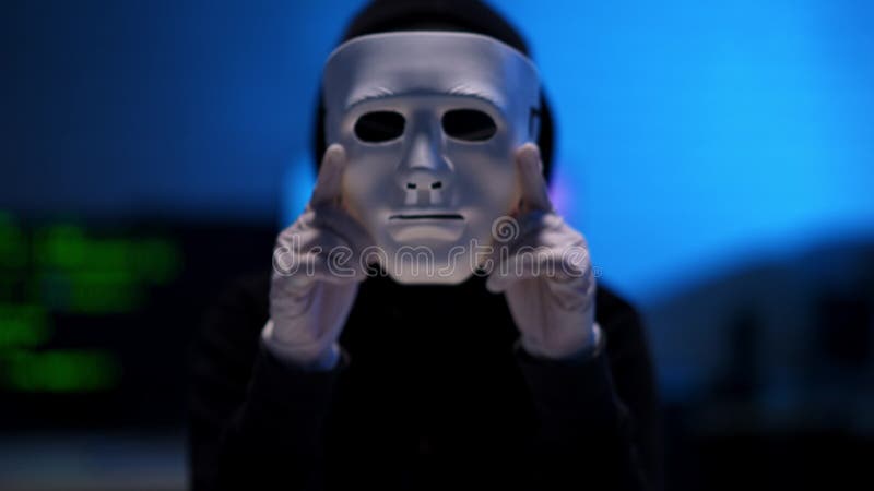 用双手戴白手套的白面罩,背景上黑客模糊. 穿着黑衣在室内的男人 股票录像