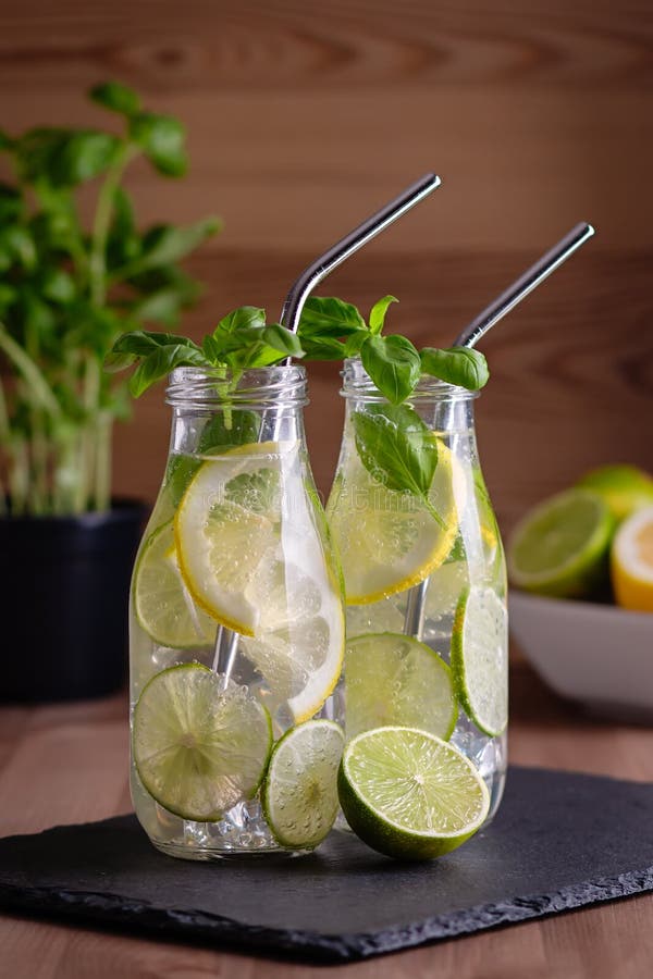 Refreshing drink or water with citrus fruits lemon and lime and basil in mason jar with reusable metal straws. Healthy lemonade drink in glass jar on kitchen table, zero waste, sustainable lifestyle. Refreshing drink or water with citrus fruits lemon and lime and basil in mason jar with reusable metal straws. Healthy lemonade drink in glass jar on kitchen table, zero waste, sustainable lifestyle