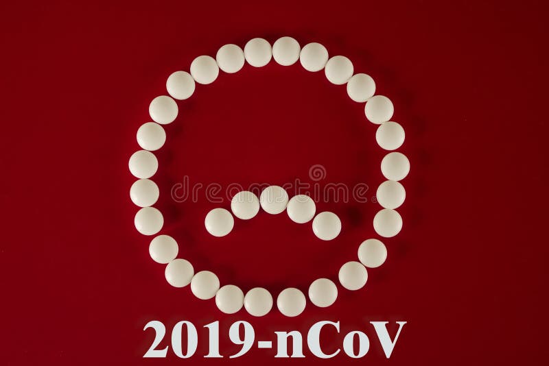 用白片和药丸制成的悲伤的笑脸,红色背景上刻有2019-nCoV,顶视图 2019年新冠状病毒 免版税库存照片 用白片和药丸制成的悲伤的笑脸,红色背景上刻有2019-nCoV,顶视图 2019年新冠状病毒 免版税库存照片