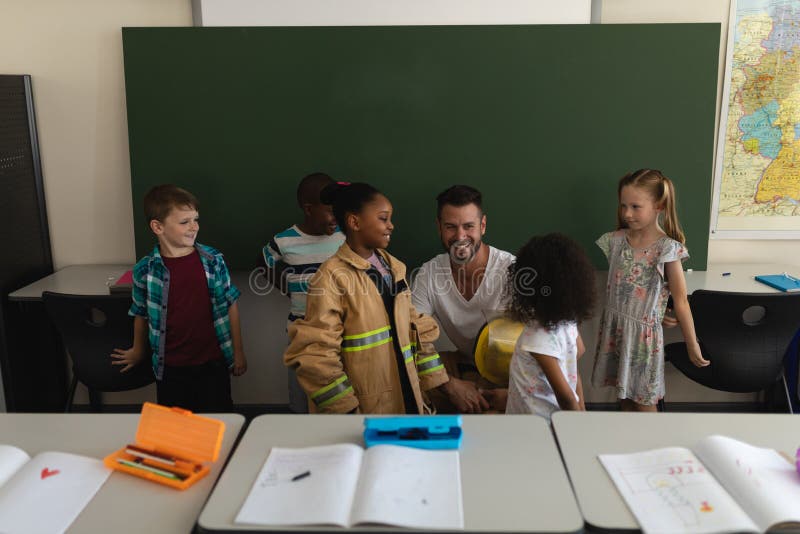 Front view of male firefighter teaching schoolkids about fire safety in classroom of elementary school. Front view of male firefighter teaching schoolkids about fire safety in classroom of elementary school