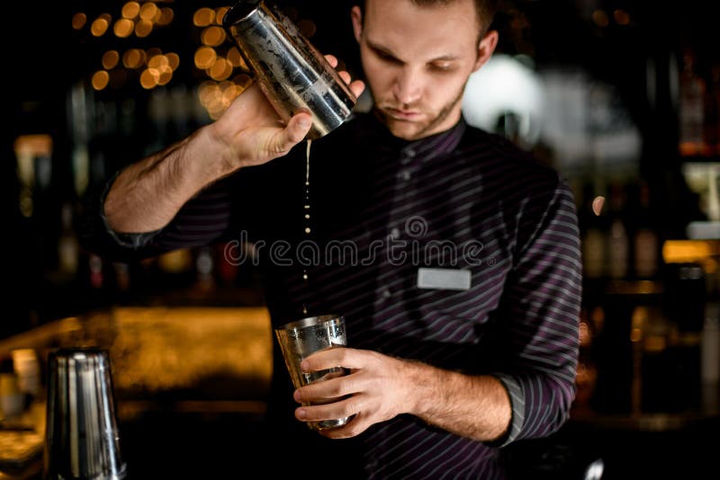 Male bartender pouring a cocktail drink from the one half of the steel shaker to another on the bar counter. Male bartender pouring a cocktail drink from the one half of the steel shaker to another on the bar counter