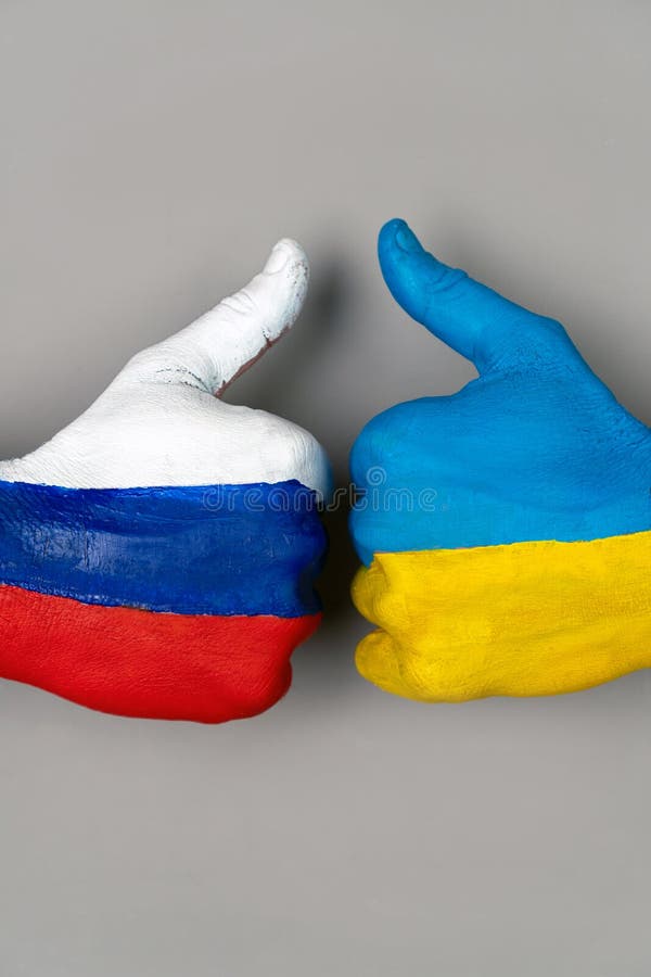 Hands painted in the flags of Ukraine and Russia raise a finger upon a gray background. Vertical. thumb up the hand of hands with the drawing of a flag. Hands painted in the flags of Ukraine and Russia raise a finger upon a gray background. Vertical. thumb up the hand of hands with the drawing of a flag.