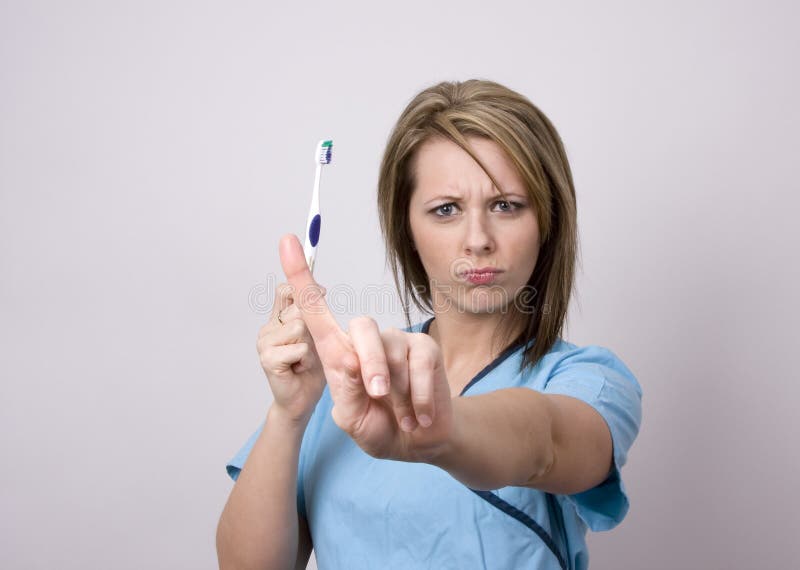 A pretty young dental assistant, holding a toothbrush, wags her finger and insists that no brushing is bad!. A pretty young dental assistant, holding a toothbrush, wags her finger and insists that no brushing is bad!