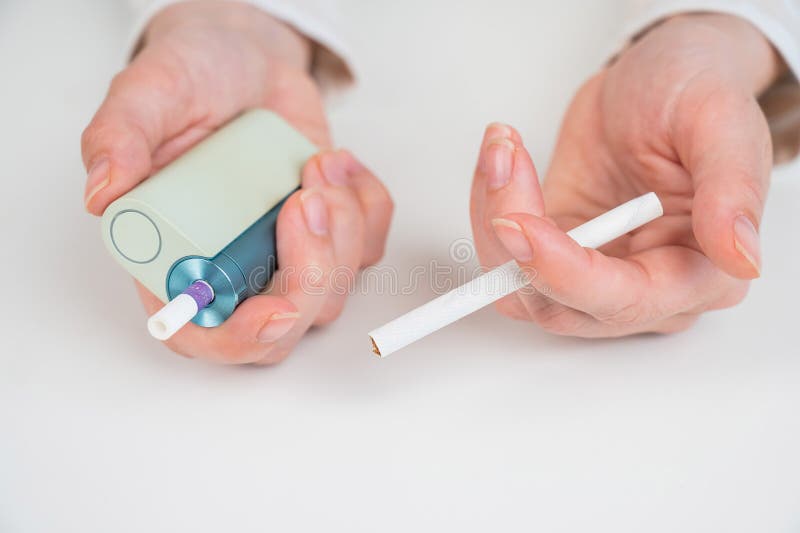 女士手持传统香烟和电子烟，背景为白色。烟草加热系统。 库存照片