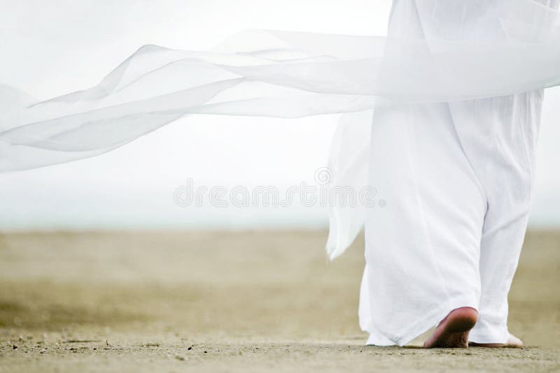 Photo of a man walking in a white robe on the sand. A picture from the back, a person is visible to the waist, clothes are fluttering in the wind. Photo of a man walking in a white robe on the sand. A picture from the back, a person is visible to the waist, clothes are fluttering in the wind