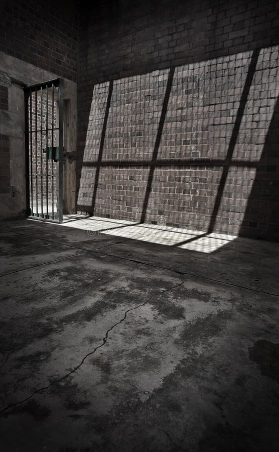 Sunlight shines through the barred door of a prison cell casting a shadow on the stone wall. Sunlight shines through the barred door of a prison cell casting a shadow on the stone wall.