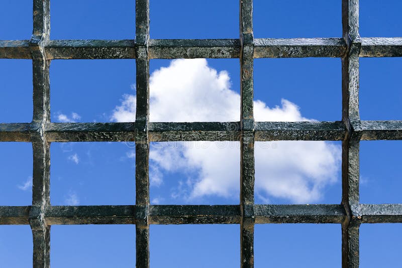 Metal jail bars with a blue sky with some clouds in the background as a concept of freedom wish. Metal jail bars with a blue sky with some clouds in the background as a concept of freedom wish