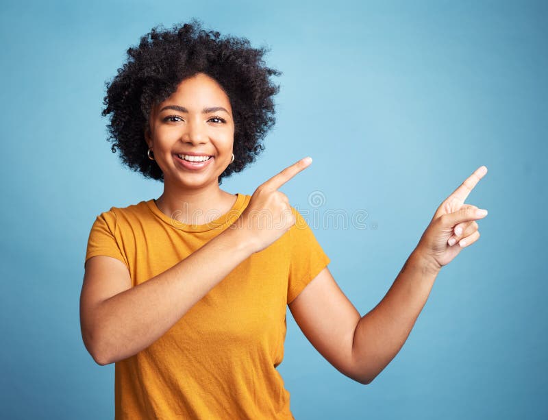 Hey, check this out. an attractive young woman standing alone against a blue background in the studio and pointing at a promotion. Hey, check this out. an attractive young woman standing alone against a blue background in the studio and pointing at a promotion