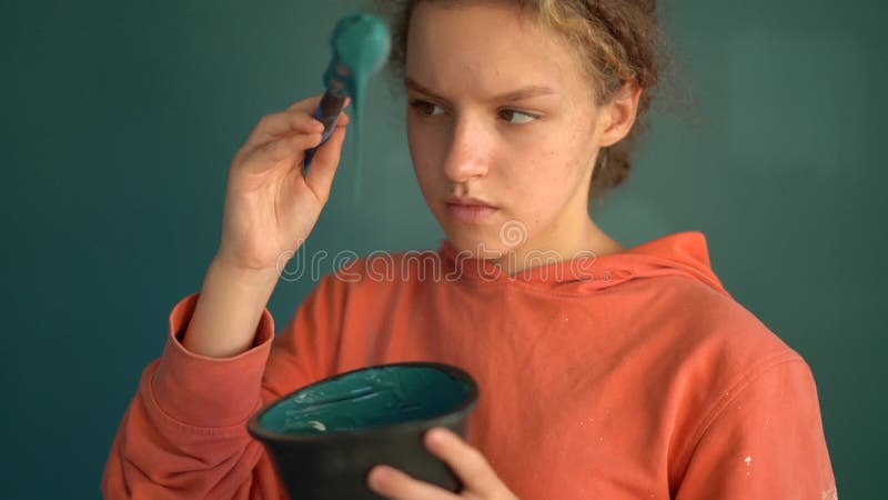 看着油漆脱落的少年. 一头卷发的红发女孩,身上有毛笔和一碗蓝色油漆 股票录像