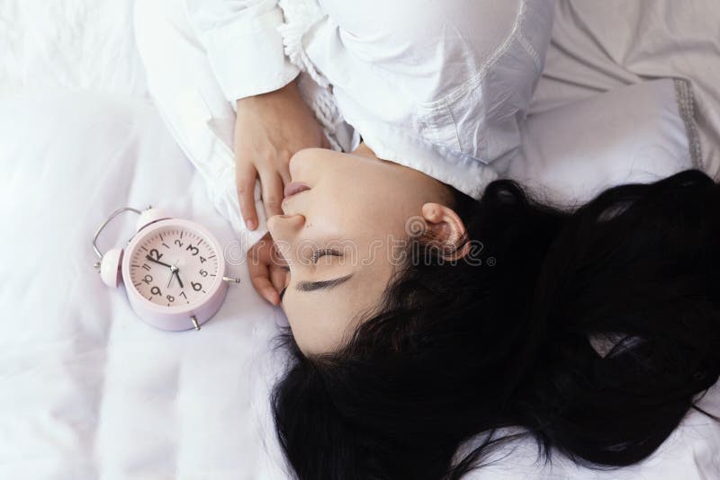 Beautiful black-haired woman sleeping in cozy bed. The alarm clock set at 7 a.m. morning. Female is going to wake up at 7 o`clock early morning. Top view to cute and sweet female. Beautiful black-haired woman sleeping in cozy bed. The alarm clock set at 7 a.m. morning. Female is going to wake up at 7 o`clock early morning. Top view to cute and sweet female