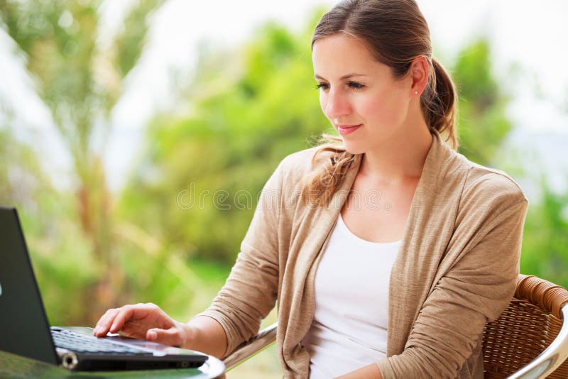 Portrait of a pretty young woman working on her computer on a terrace of her house - paying online with her credit card. Portrait of a pretty young woman working on her computer on a terrace of her house - paying online with her credit card