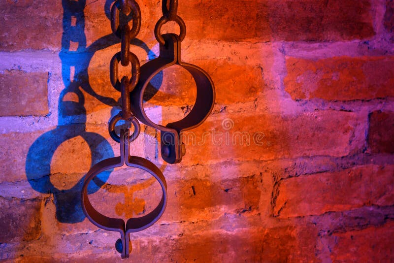 Old iron chains and shackles on a red brick wall lit in red-blue light. Old iron chains and shackles on a red brick wall lit in red-blue light