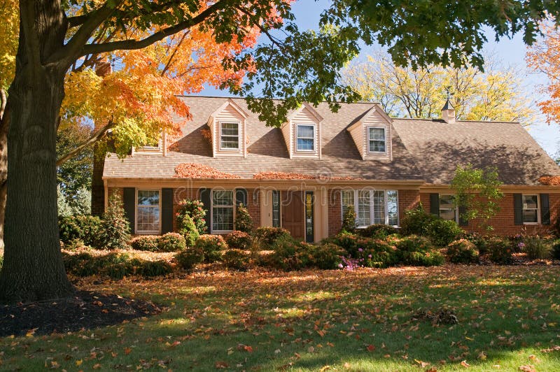 A view of a comfortable brick house with colorful autumn leaves on a bright fall day. A view of a comfortable brick house with colorful autumn leaves on a bright fall day.