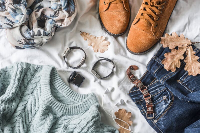 Flat lay women`s clothing for autumn walks, top view. Brown suede boots, jeans, a blue pullover, scarf, bracelets, watches, headphones, perfume on a light background. Fashion concept. Flat lay women`s clothing for autumn walks, top view. Brown suede boots, jeans, a blue pullover, scarf, bracelets, watches, headphones, perfume on a light background. Fashion concept