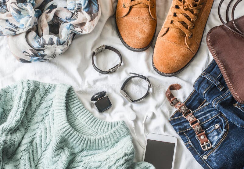 Flat lay women`s clothing for autumn walks, top view. Brown suede boots, jeans, a blue pullover, scarf, bracelets, watches, headphones, perfume and bag on a light background. Fashion concept. Flat lay women`s clothing for autumn walks, top view. Brown suede boots, jeans, a blue pullover, scarf, bracelets, watches, headphones, perfume and bag on a light background. Fashion concept