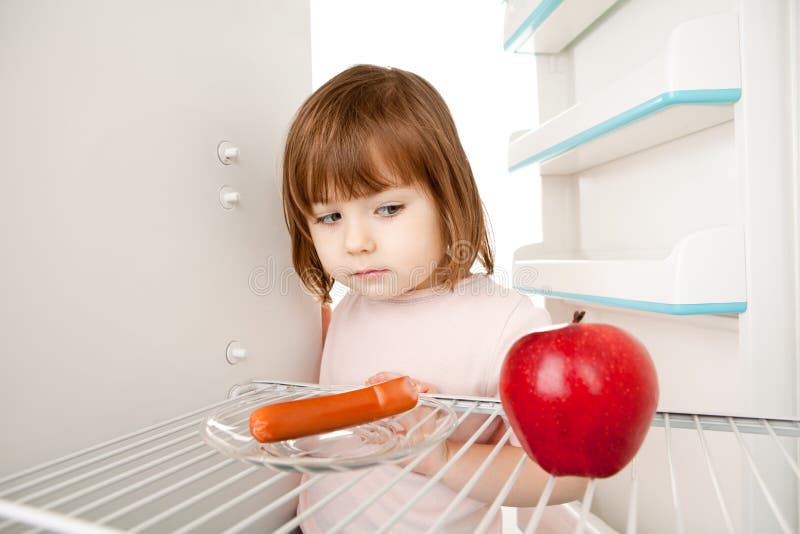 Girl looking in an almost empty refrigerator seeing an apple and hot dog. Girl looking in an almost empty refrigerator seeing an apple and hot dog.