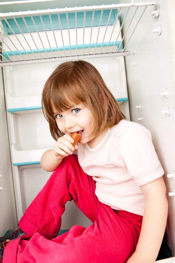 Young girl sitting in an empty refrigerator eating a hot dog. Young girl sitting in an empty refrigerator eating a hot dog.