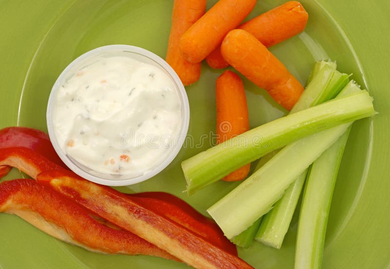 A close view of several pieces of red pepper, baby carrots, celery and ranch dressing on a green plate. A close view of several pieces of red pepper, baby carrots, celery and ranch dressing on a green plate.