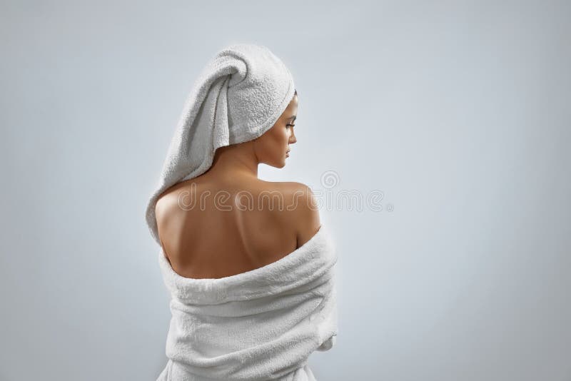 Back view of pretty female with towel on head and in bathrobe posing, looking over shoulder. Portrait of woman enjoying time after fresh shower, isolated on grey background. Beauty, skincare concept. Back view of pretty female with towel on head and in bathrobe posing, looking over shoulder. Portrait of woman enjoying time after fresh shower, isolated on grey background. Beauty, skincare concept.