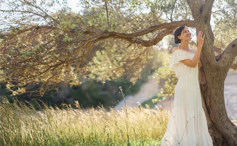 Beautiful Asian young woman in white dress outdoor near olive tree. embracing fresh air and engaging in outdoor activities. Friluftsliv concept means spending as much time outdoors as possible. Beautiful Asian young woman in white dress outdoor near olive tree. embracing fresh air and engaging in outdoor activities. Friluftsliv concept means spending as much time outdoors as possible