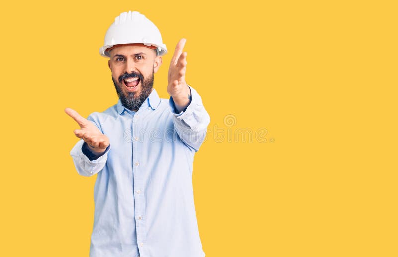 穿着建筑师硬帽的年轻帅哥看着镜头微笑着拥抱 库存图片