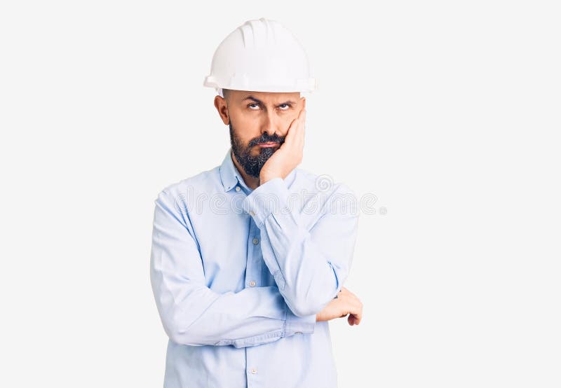 穿着建筑师硬帽的年轻英俊男子看上去疲惫不堪，双臂交叉让他厌倦抑郁 免版税库存图片