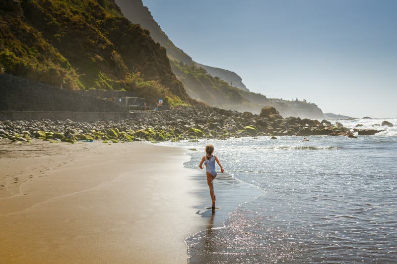 穿着泳装的小女孩在海浪旁的沙滩上欢快地奔跑，在她脚下的Playa del Socorro Tenerife海滩上 库存图片