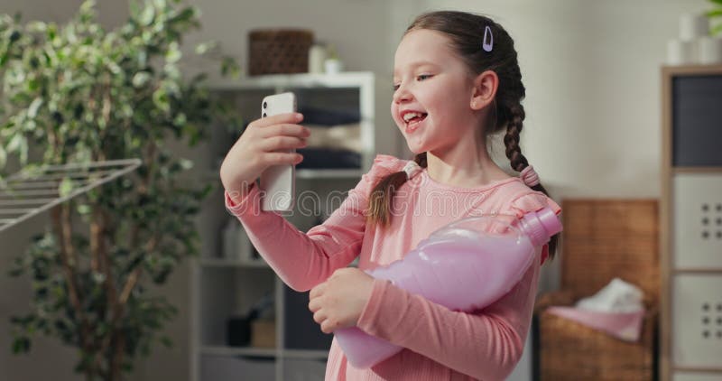 穿着粉红色裙子的小女孩站在洗衣间浴室的正中,拿着漂洗液,她在视频中给她妈妈打电话 股票视频