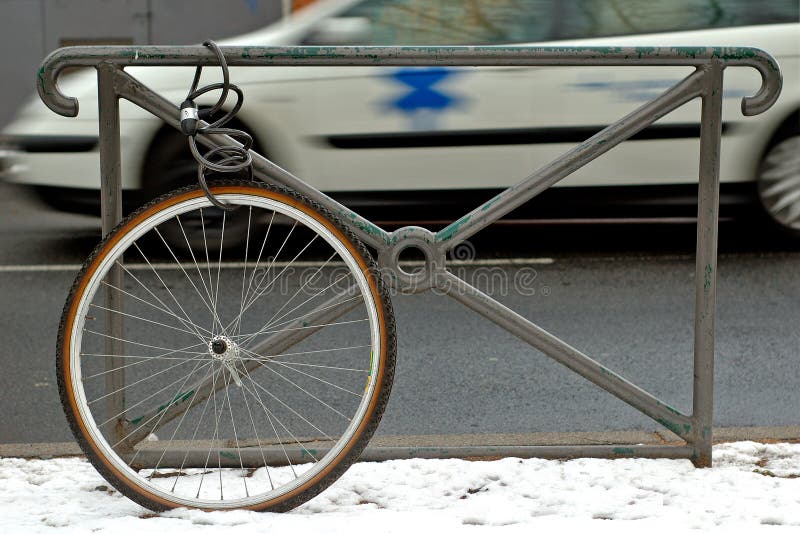 Bicycle wheel locked alone to a gate. In the background, an ambulance. Bicycle wheel locked alone to a gate. In the background, an ambulance.