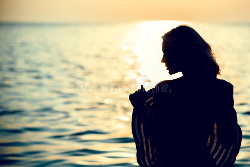 Silhouette of a beautiful woman standing with her back to the camera in the sea water at sunrise holding a large wide-brimmed hat in front of her body. Copy space. Silhouette of a beautiful woman standing with her back to the camera in the sea water at sunrise holding a large wide-brimmed hat in front of her body. Copy space