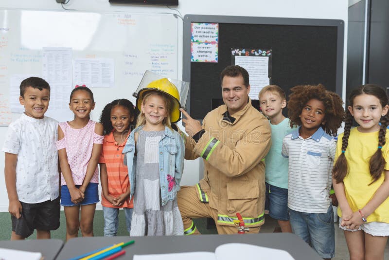 Portrait of happy school kids standing with firefighter in classroom at school agaisnt a blackboard and a whiteboard in background. Portrait of happy school kids standing with firefighter in classroom at school agaisnt a blackboard and a whiteboard in background