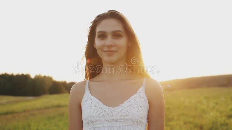 站立在一个草甸的俏丽的妇女在夏天晚上 流动在风的长的头发在阳光下在日落