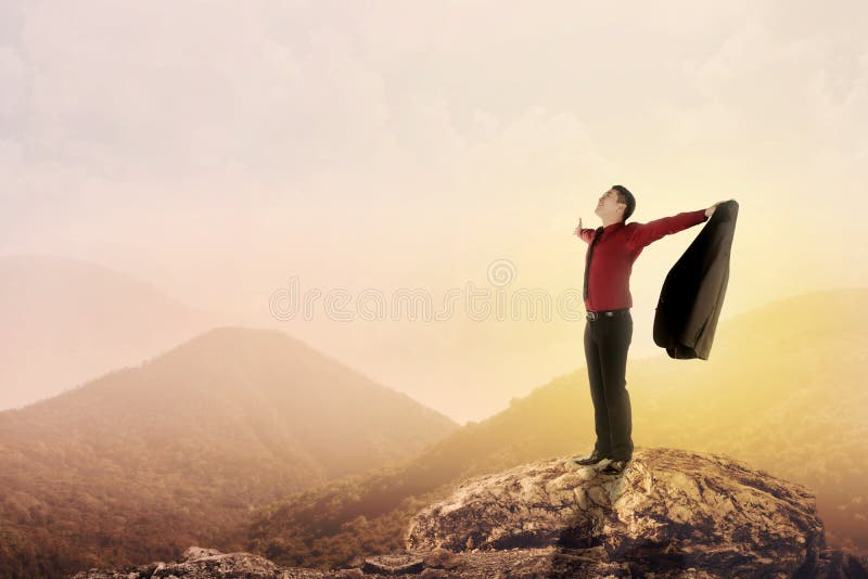 Asian business man standing on the top of mountain, raise hand and open his suit. Asian business man standing on the top of mountain, raise hand and open his suit