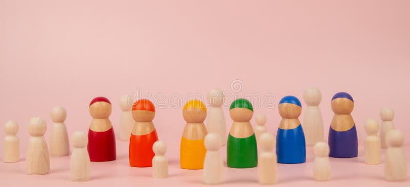 粉红色背景中未涂漆的木雕中，矗立着彩虹色木人雕像. LGBTQIA团队合作自豪感 库存照片