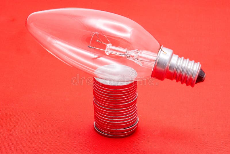红色背景上一叠硬币上的灯泡. 节约电费和经济联系 免版税库存图片