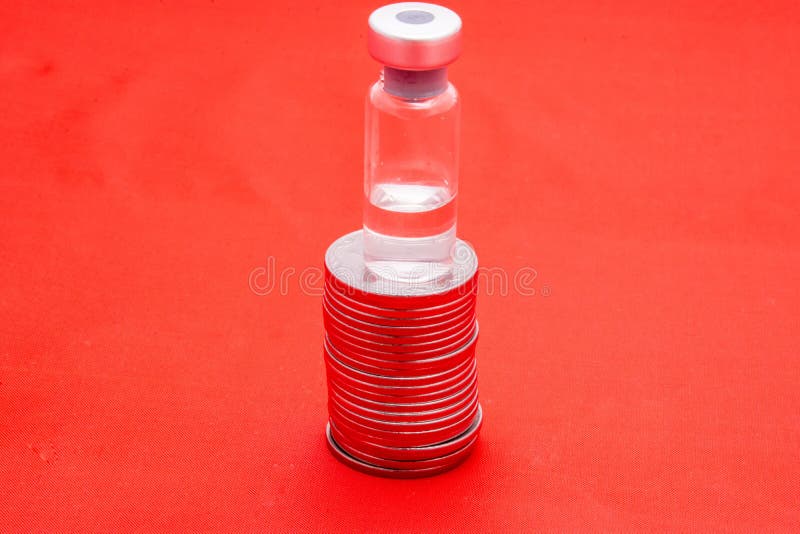 红色背景上的硬币堆放着透明药瓶. 药品成本药品公司开发 库存图片