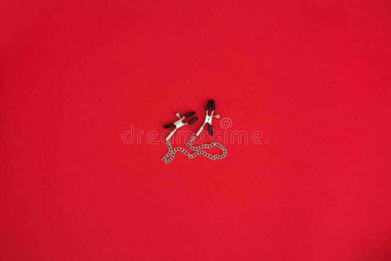 Nipple clamps in red background. BDSM outfit. Accessories for adult sex games. Nipple clamps in red background. BDSM outfit. Accessories for adult sex games.