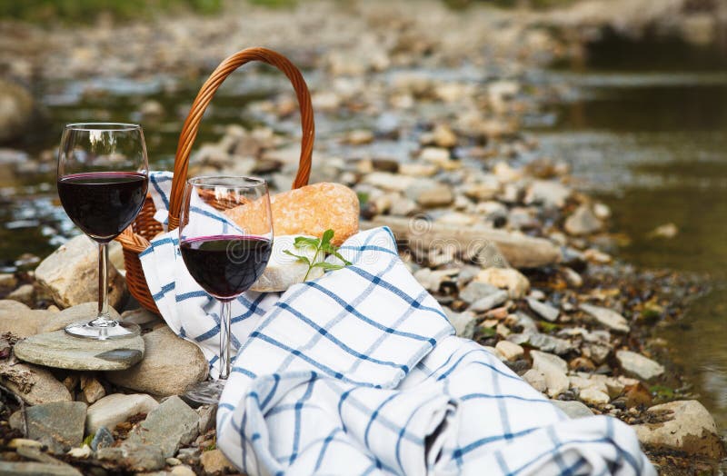 Red wine, cheese and bread served at a picnic. Mountain river background. Red wine, cheese and bread served at a picnic. Mountain river background