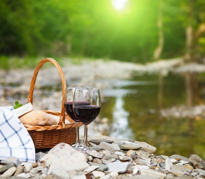 Red wine, cheese and bread served at a picnic. Mountain river background. Red wine, cheese and bread served at a picnic. Mountain river background