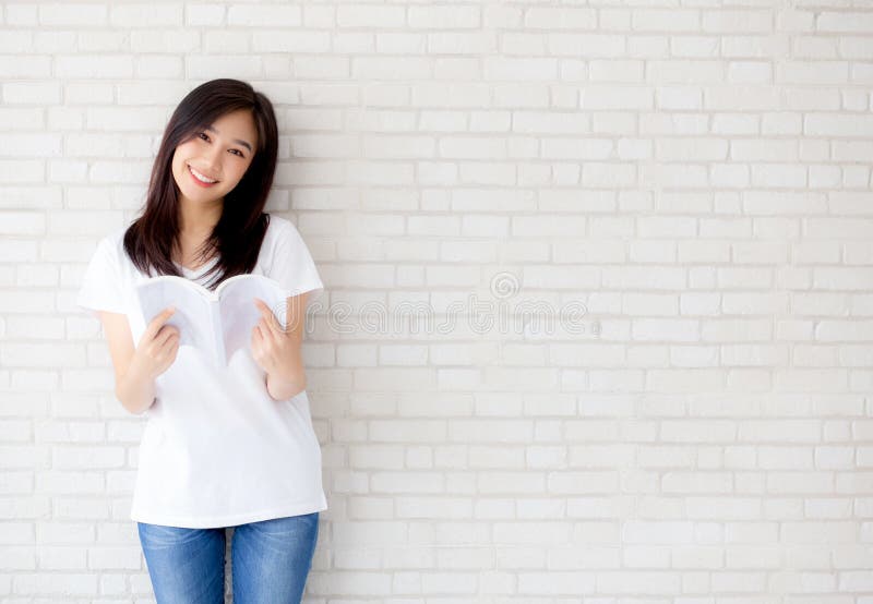 美丽画象年轻亚洲妇女幸福放松在具体水泥白色背景的常设阅读书 免版税库存图片 美丽画象年轻亚洲妇女幸福放松在具体水泥白色背景的常设阅读书 免版税库存图片