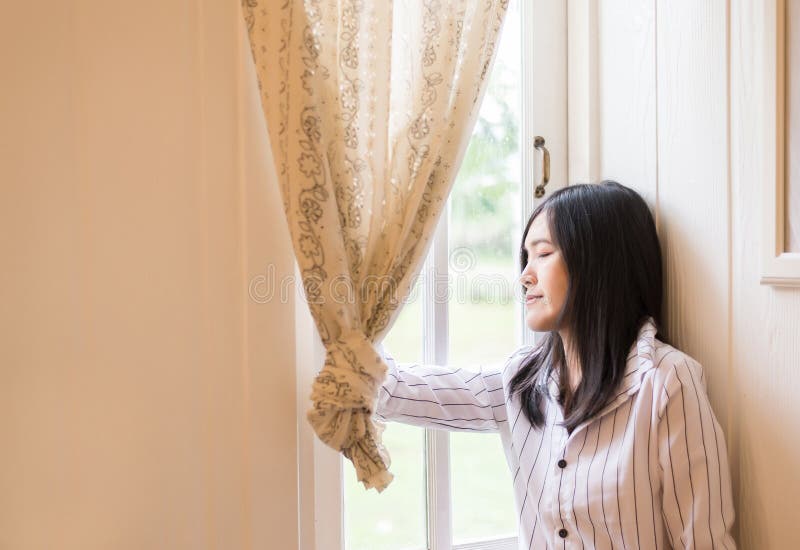 美丽的亚裔女性画象放松,并且在家站立在窗口附近,正面认为,好态度,闭上您的眼睛 免版税库存照片 美丽的亚裔女性画象放松,并且在家站立在窗口附近,正面认为,好态度,闭上您的眼睛 免版税库存照片
