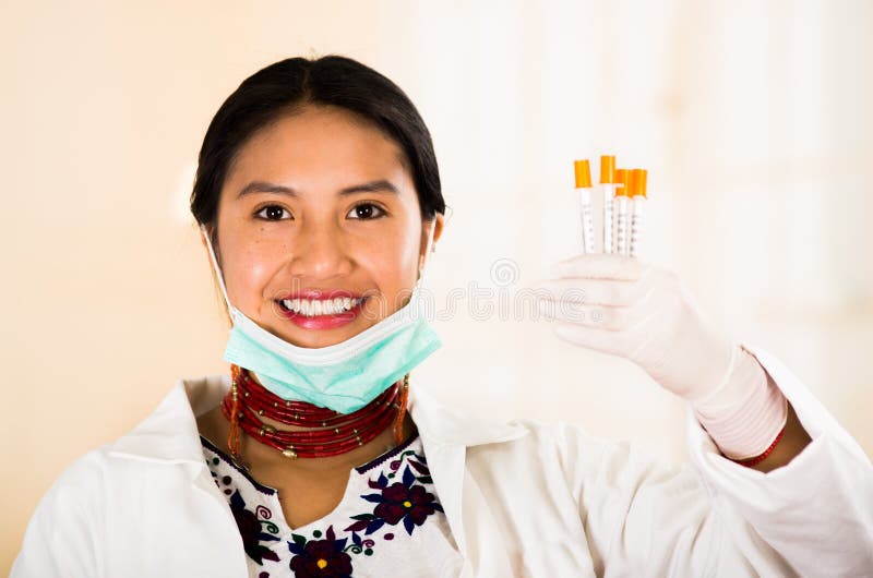 年轻美丽的妇女在医生穿戴了涂上和红色项链，面部面具被拉下对下巴，阻止注射器 免版税库存照片