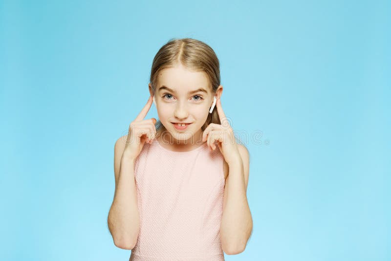 美丽的小女孩通过无线耳机听音乐 看着摄象机的女孩 蓝色背景中的肖像 库存照片 美丽的小女孩通过无线耳机听音乐 看着摄象机的女孩 蓝色背景中的肖像 库存照片