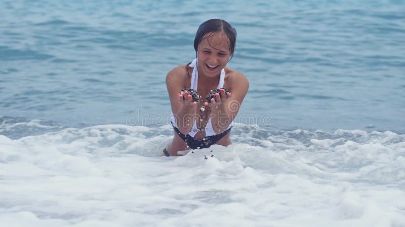 美丽的比基尼泳装的年轻逗人喜爱的妇女在水中坐海岸通过手洒木瓦，飞溅水和
