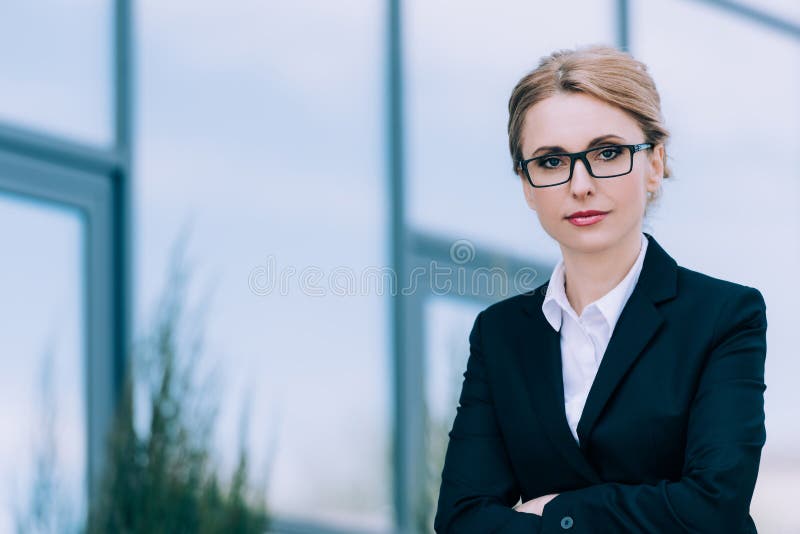 美好的中部变老了站立与横渡的胳膊和看照相机的镜片的女实业家 图库摄影
