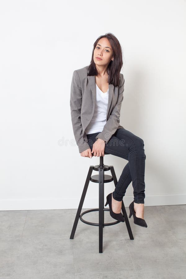 Female self-employment - beautiful young professional woman sitting on a stool posing for her first job over sparse white background. Female self-employment - beautiful young professional woman sitting on a stool posing for her first job over sparse white background