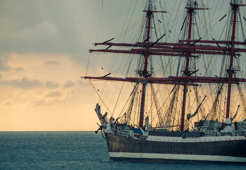 Old sailing ship against sunset. Ancient sailboat on a stormy sky background. Historic three-masted sailing ship. Nautical landscape - sea voyage at old tall ship. Old sailing ship against sunset. Ancient sailboat on a stormy sky background. Historic three-masted sailing ship. Nautical landscape - sea voyage at old tall ship.